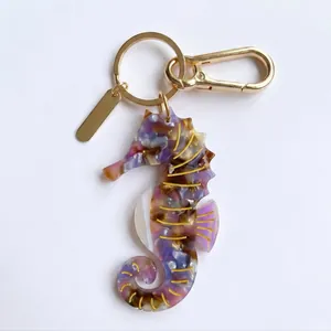 Detalle del llavero de caballito de mar de acrílico morado veteado con dorado.