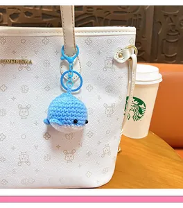 Adorable handmade blue crocheted whale keychain accessory hanging on a white textured handbag