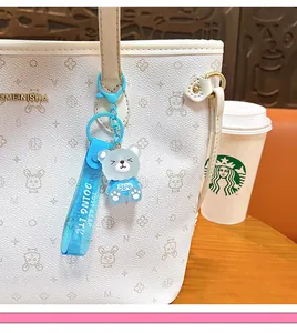 Detail view of a cute blue jelly bear keychain charm attached to a white textured handbag