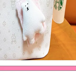 Detailed close-up of a white plush bear mirror keychain charm attached to a cream handbag