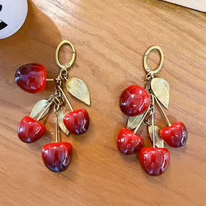 Elegante coppia di portachiavi a ciliegia rossa con foglie dorate su tavolo in legno
