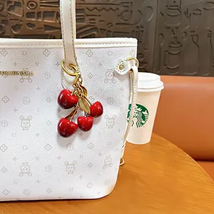 Elegante portachiavi con ciliegia rossa e foglie dorate presentato su una borsa bianca chic