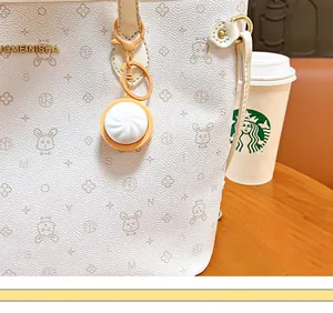 Detail view of a glowing xiaolongbao charm hanging on a cream patterned handbag