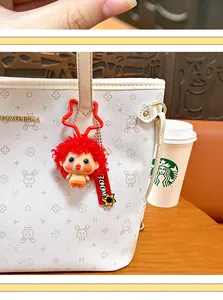 Close-up of a creative red frizzy hair doll keychain charm hanging on a white fashion tote bag