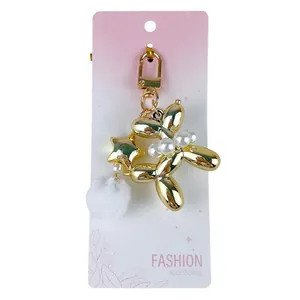 Elegant gold-plated balloon dog keychain with white pearls and fluffy pom-pom on gift card