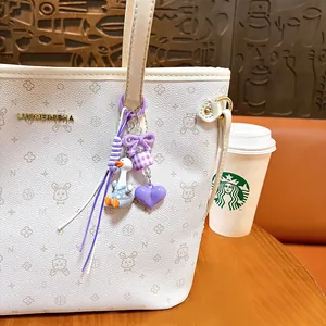 Cute duck bag charm keychain with purple bow and heart pendant on a white patterned bag