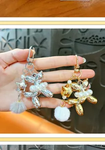 Detailed view of silver and gold balloon dog keychains with pearls and fluffy pom-poms.