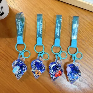 Four ocean-themed shell liquid keychains with glitter and charms on a wooden surface.