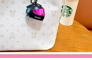Detailed macro view of a miniature black motorcycle helmet keychain pendant on a white bag