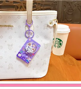 Close-up of a purple cartoon dice machine keychain hanging on a white handbag