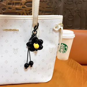 Elegante ciondolo a fiore nero appeso a una borsa bianca in un ambiente da caffè
