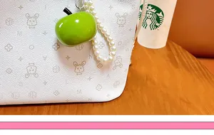Detail view of a green resin apple keychain with pearl beads attached to a bag