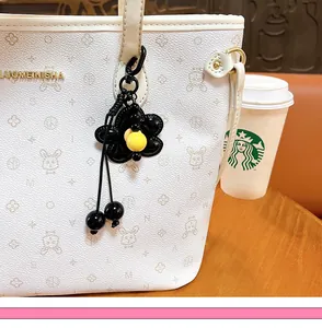 Dettaglio del ciondolo per borsa a fiore nero con perla gialla su borsa bianca