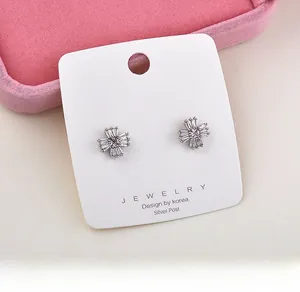 Elegant silver flower stud earrings with baguette crystals on a white jewelry display card