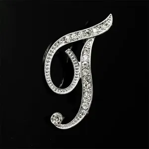 Vista detallada del elegante broche de letra T plateado con diamantes de imitación