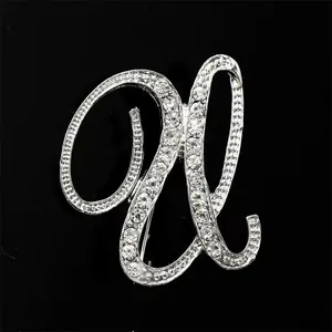Primer plano de un broche de letra plateado con brillantes strass sobre fondo negro