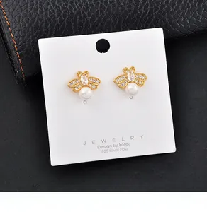 Macro view of gold bee-shaped stud earrings featuring pearls and crystals on white jewelry card