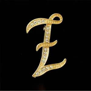Vista detallada de un elegante broche con la letra E dorada y brillantes pedrería para mujer.