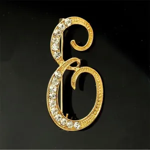 Vista detallada de un broche con letra E dorada y brillantes diamantes de imitación.