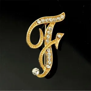 Detalle macro de un broche dorado con forma de F incrustado con brillantes pedrería blanca