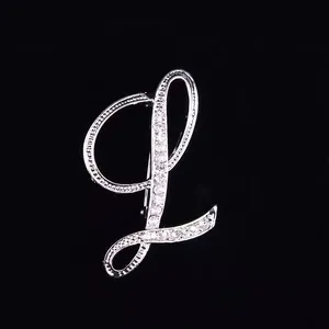 Vista detallada de un broche plateado con letra L cursiva y diamantes de imitación