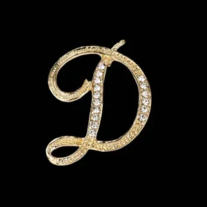 Vista detallada de un brillante broche dorado con la letra D y diamantes de imitación.