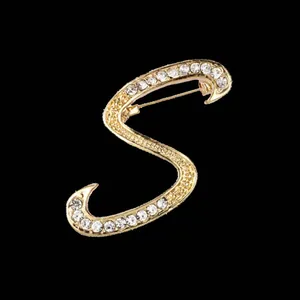 Detalle de primer plano de un broche de letra S dorado con brillantes piedras de strass
