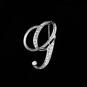 Vista detallada de un elegante broche plateado en forma de letra G cursiva con diamantes