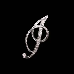 Primer plano de un broche de letra plateado con diamantes de imitación en fuente cursiva.