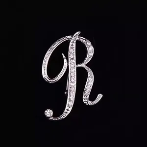 Vista detallada de un broche plateado con forma de letra R y brillantes de imitación
