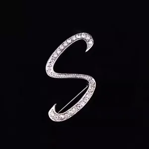 Primer plano de un elegante broche plateado con la letra S y brillantes cristales de strass