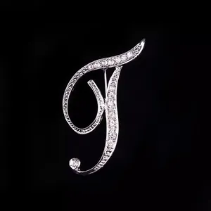 Primer plano de un elegante broche plateado con la letra T y cristales