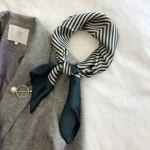 Elegant green and white striped silk square neck scarf styled on a coat with a pearl brooch