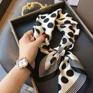 Close-up of a black and white polka dot silk-like square scarf held by hand in a tray