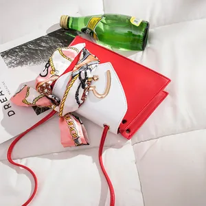 Close-up of a red and white mini square bag with a golden heart buckle and silk scarf