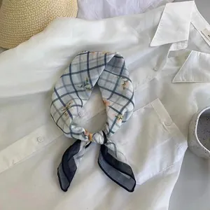 Dettaglio di un foulard in seta con stampa floreale e a quadri su camicia bianca.
