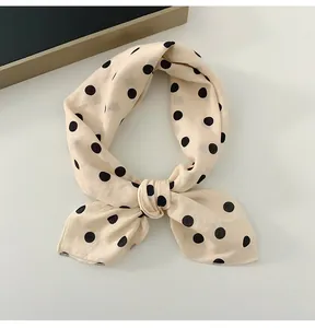 Close-up of a cream cotton linen square scarf with black polka dots tied in a knot