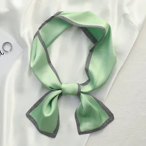 Detail view of light green silk scarf with black white striped border tied in bow.