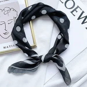 Dettaglio di un foulard quadrato a pois bianco e nero annodato come un fazzoletto