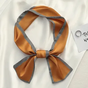 Close-up of a ginger silk twilly scarf with a black and white striped border