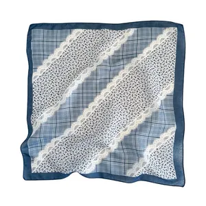 Dettaglio di un foulard quadrato a quadri blu con motivi floreali bianchi e pizzo.