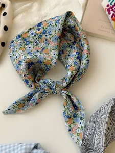 Detail shot of a blue floral cotton linen square scarf tied in a knot on white desk