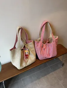 Vue détaillée de deux sacs cabas en paille tissée et toile à carreaux rouges sur un banc