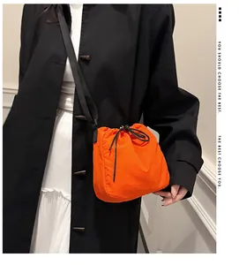 Vibrant orange nylon drawstring bucket bag featuring a sleek black crossbody strap detail