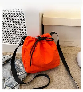 Close-up detail of a bright orange nylon drawstring bucket bag with black shoulder strap
