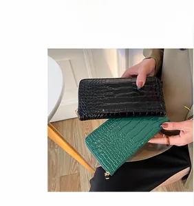Primer plano de carteras largas negras y verdes con grabado de cocodrilo y cremallera.