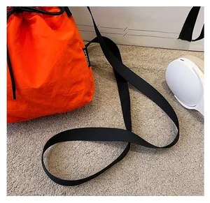 Detail showing the durable black nylon strap and vibrant orange fabric of the bucket bag