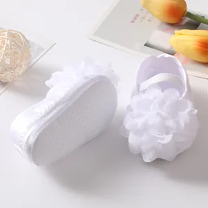 Détail de chaussures de princesse pour bébé blanches avec fleur en tissu et semelle antidérapante