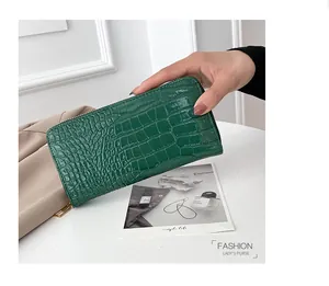 Vista detallada de un bolso de mano verde para mujer con relieve de cocodrilo en la mano.
