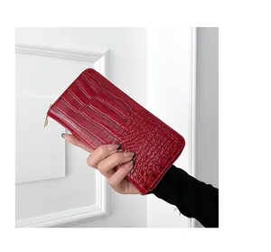 Primer plano de una mano sosteniendo una cartera larga de cuero PU rojo con grabado de cocodrilo
